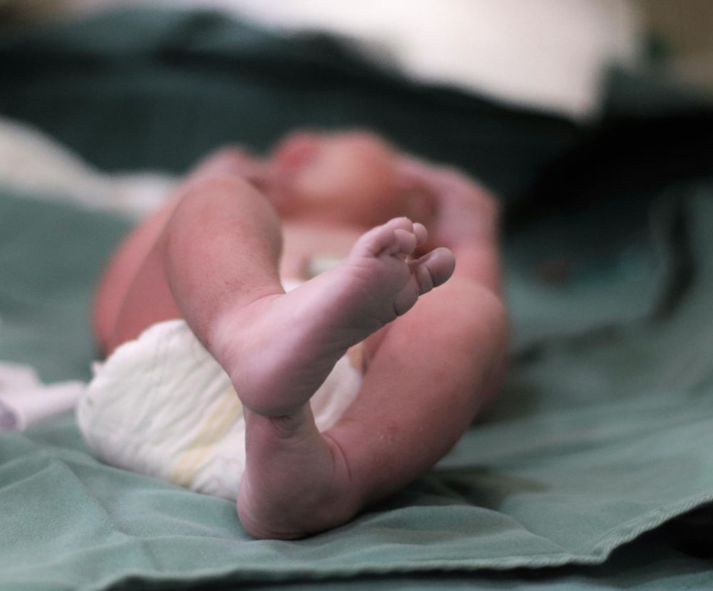 Neugeborenes Baby liegt entspannt zusammengerollt auf einem grünen Tuch, kurz nach der Geburt